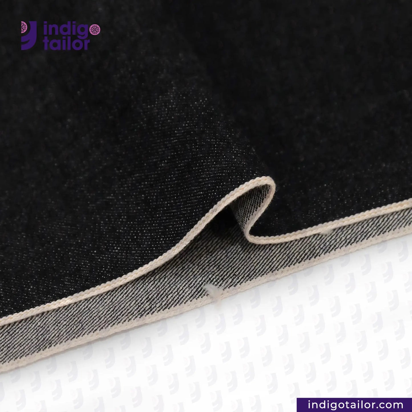 Close-up of BLACK SLUBBY SELVEDGE DENIM fabric with beige edge on a white background, featuring Indigotailor logo.