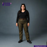 Woman wearing a black top and green pants with 'Indigo Tailor' branding on a gray background. BULLION GOLD SELVEDGE DENIM