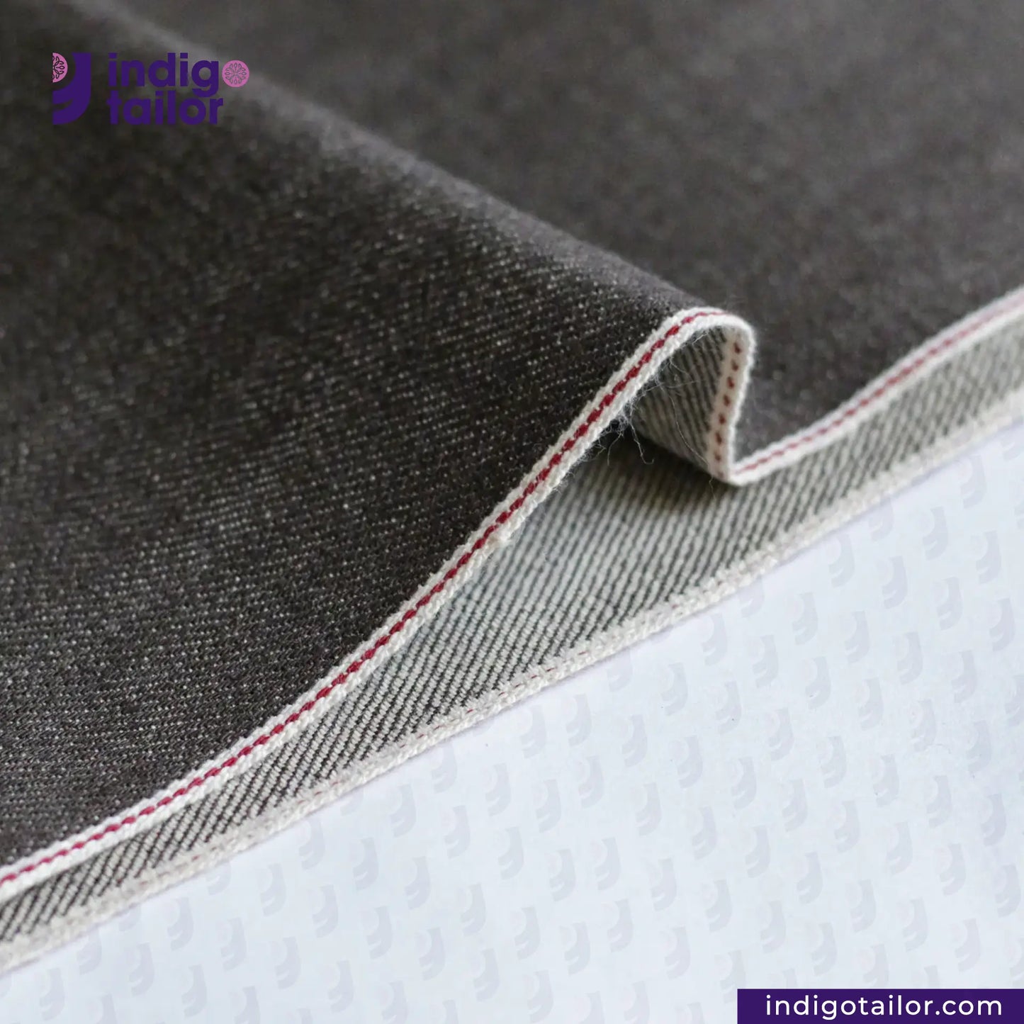 Close-up of gray denim fabric with a visible brand logo and website. Brown SOFT SLUB SELVEDGE DENIM
