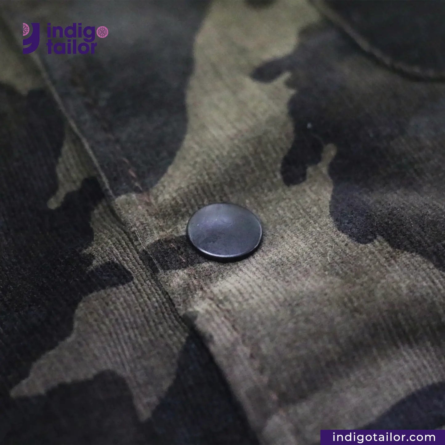 Close-up of a button on a CORD CAMO OVERSHIRT camouflage jacket with 'Indigotailor' branding.