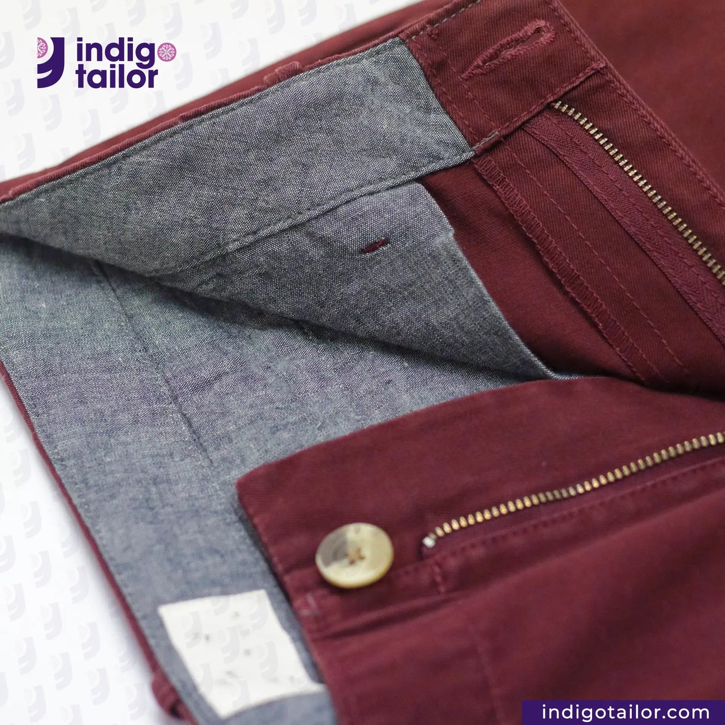 Close-up of Chino Burgundy fabric with a button and zipper, branded 'Indigotailor'.