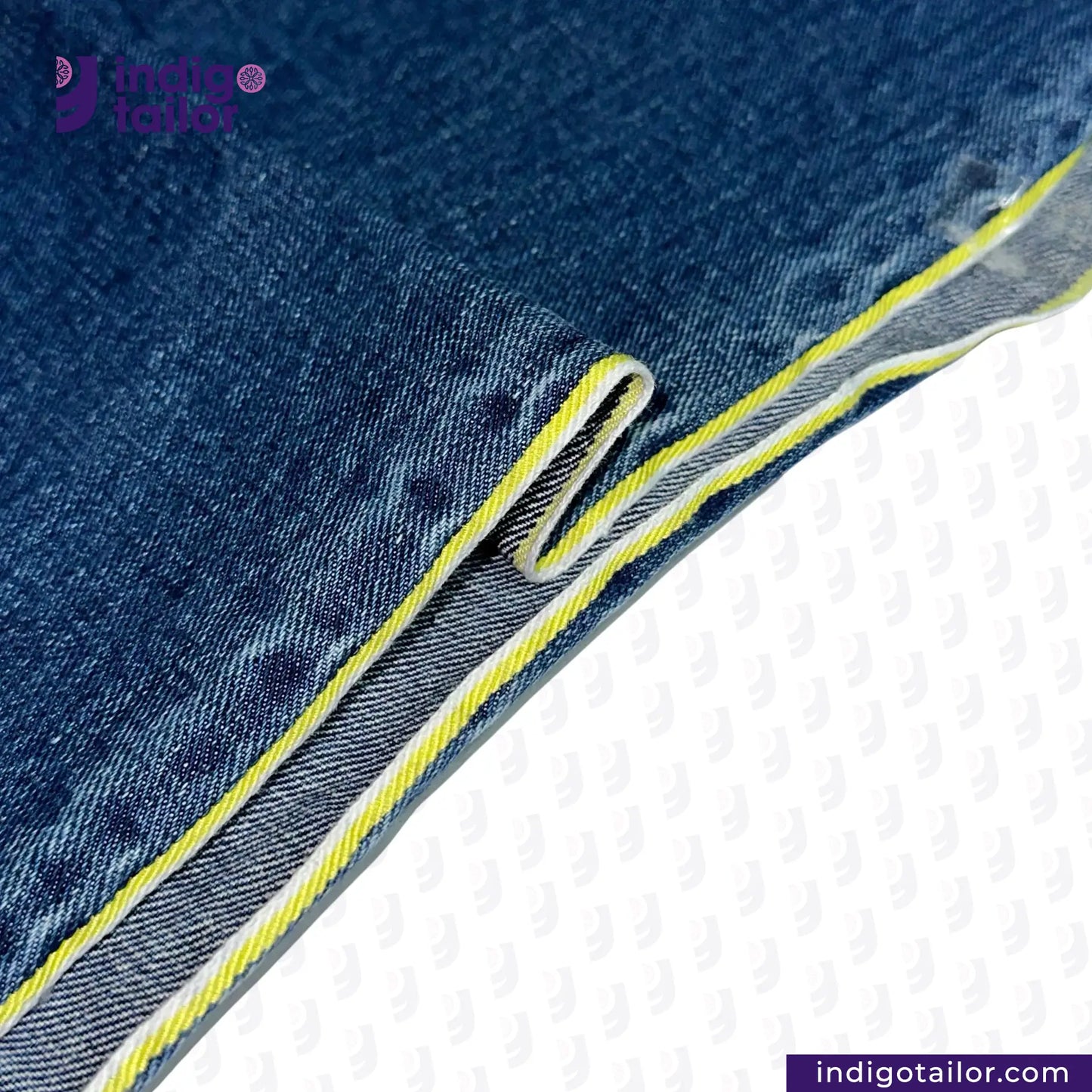 Close-up of DARK WASHED SELVEDGE DENIM LIME SELVEDGE fabric with yellow stitching on a white background, featuring the Indigo Tailor logo.