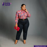 Woman wearing a floral blouse and DEEP INDIGO GREENCAST SELVEDGE DENIM pants with a red clutch, standing against a gray background with 'Indigotailor' branding.