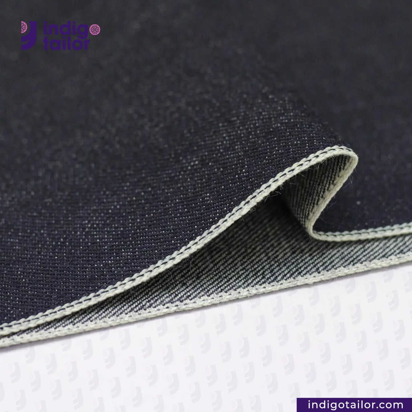 Close-up of DEEP INDIGO GREENCAST SELVEDGE DENIM fabric with a visible brand logo on a white background
