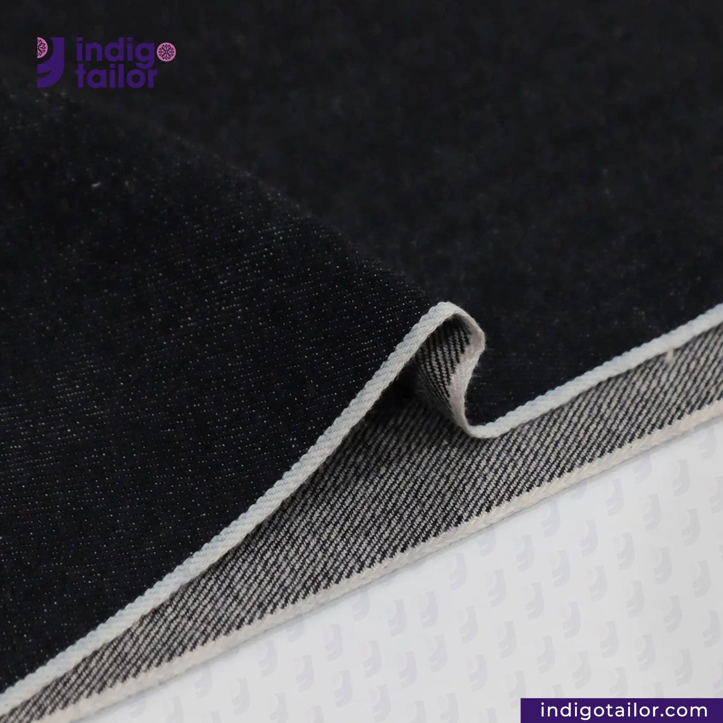 DEEP INDIGO OMBRÉ CAST DENIM fabric with gray stitching on a textured surface, featuring the Indigotailor logo.