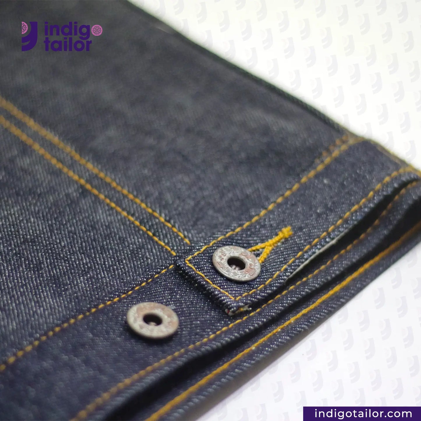 Close-up of DENIM BIKER VEST Cuff with yellow stitching and a button, branded 'Indigotailor'.