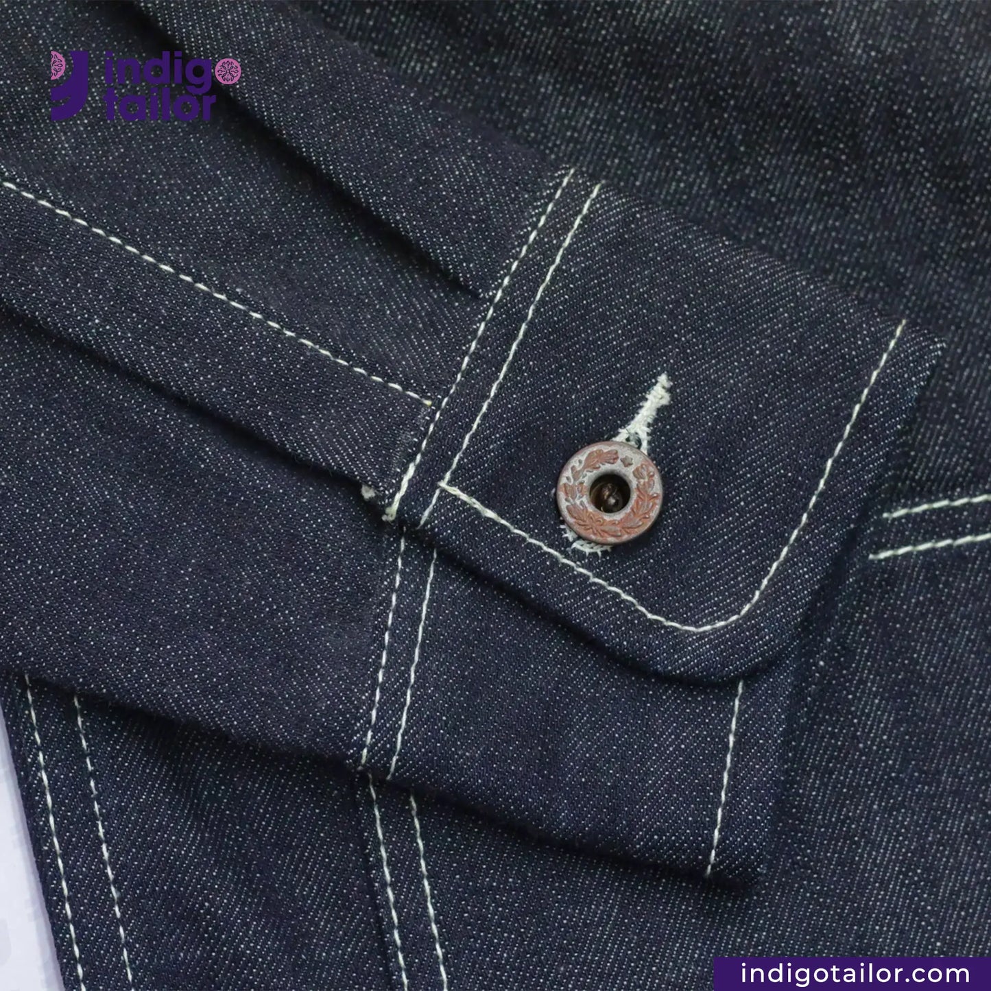 Close-up of a DENIM CHORECOAT shirt pocket with a button, featuring 'Indigotailor' branding.