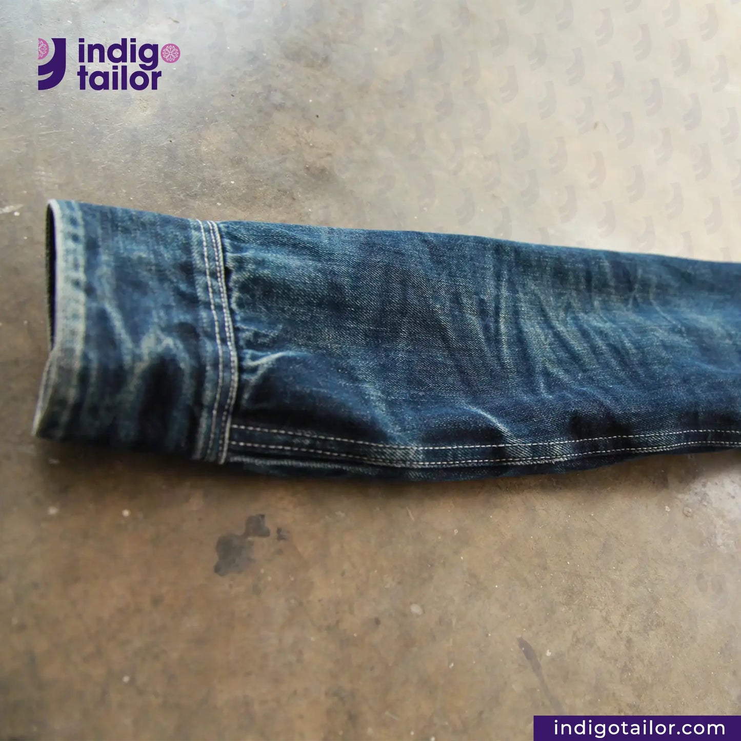Rolled-up DENIM CHORECOAT on a metallic surface with 'indigotailor' branding.