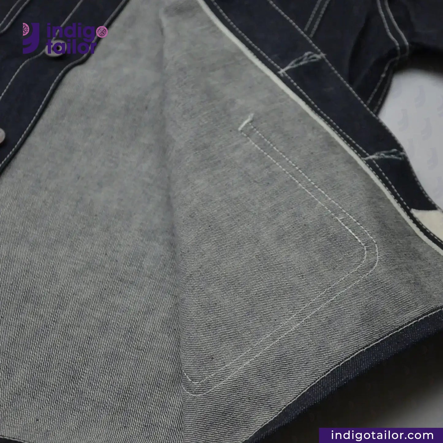 Close-up of DENIM CHORECOAT fabric with stitching detail, featuring the Indigo Tailor logo.
