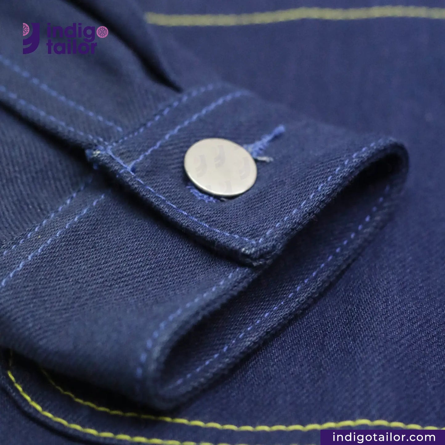 Close-up of a DOUBLE DIPPED TRIPLE PLEAT REPRO fabric with a button and yellow stitching, featuring the Indigotailor logo.