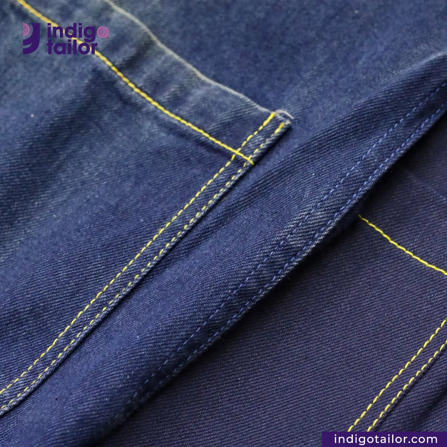 Close-up of DOUBLE DIPPED TRIPLE PLEAT REPRO denim fabric with yellow stitching, featuring the Indigotailor logo.