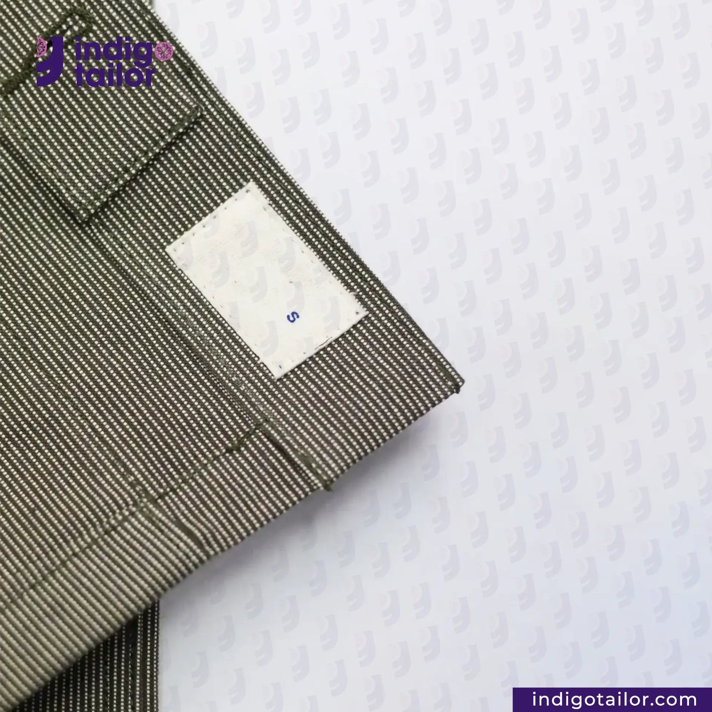 Close-up of a EASY JACKET OLIVE WABASH ONE WASH with a white label on a textured white background, featuring the brand 'indigotailor'.