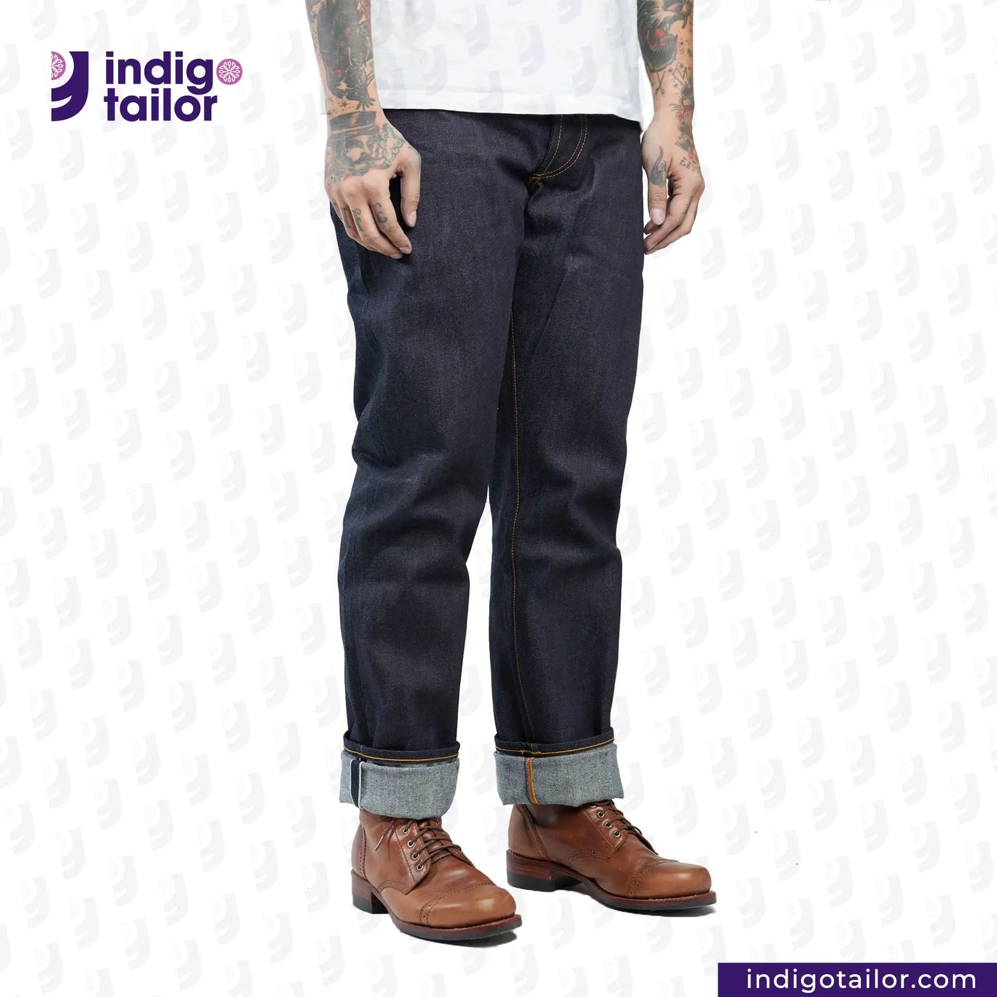 Person wearing dark blue jeans with rolled-up cuffs and brown shoes on a white background, with 'Indigo Tailor' logo.