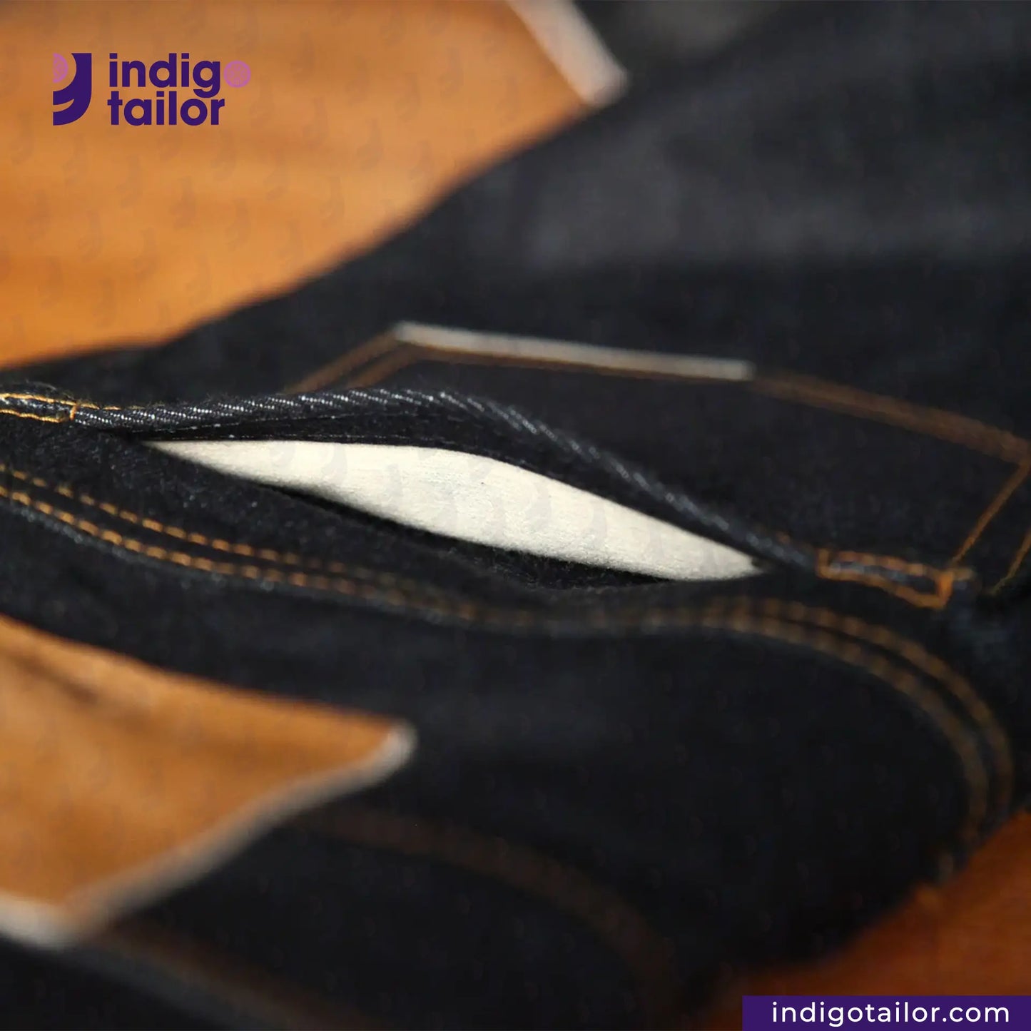 Close-up of dark denim fabric with 'indigotailor' branding.