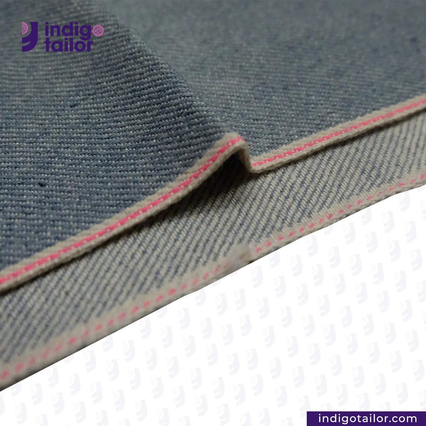 Close-up of ICE BLUE SELVEDGE DENIM fabric with pink stitching on a white background, featuring the Indigotailor logo.