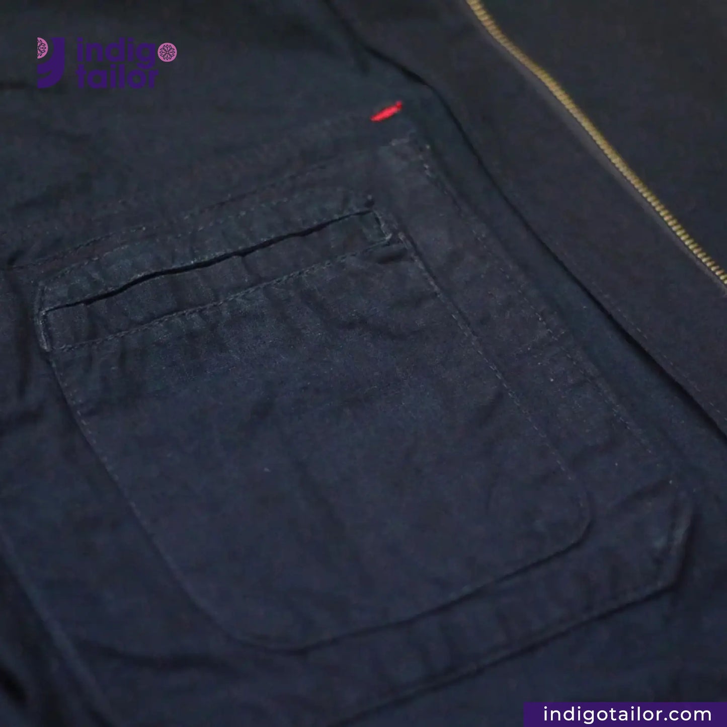 Close-up of a INDIGO HARRINGTON JACKET with a pocket and zipper, featuring the brand 'Indigo Tailor'.