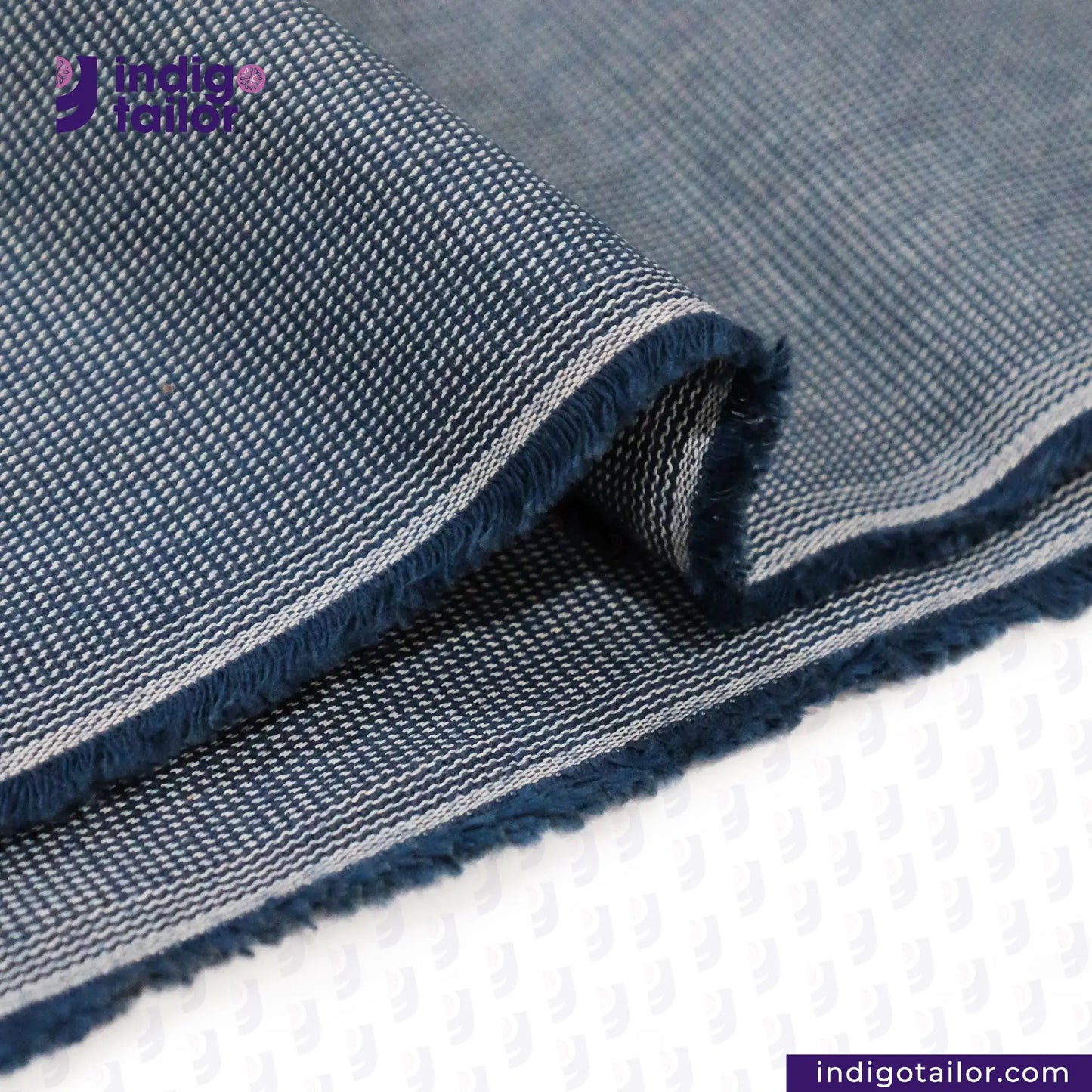 Close-up of INDIGO HOUNDSTOOTH denim fabric with 'Indigo Tailor' logo and website.