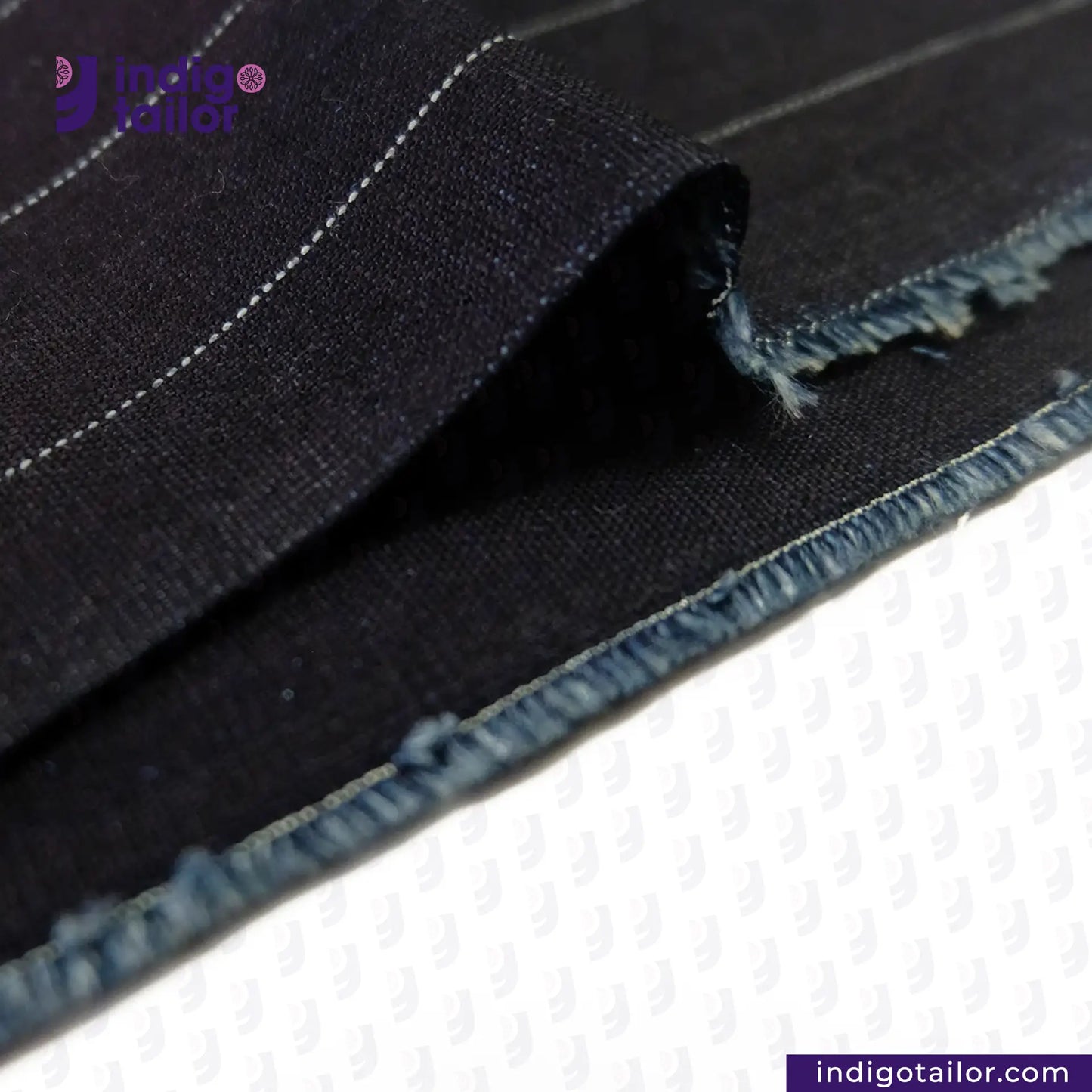 Close-up of INDIGO PINSTRIPES denim fabric with visible stitching on a white background, featuring the 'indigotailor' brand.
