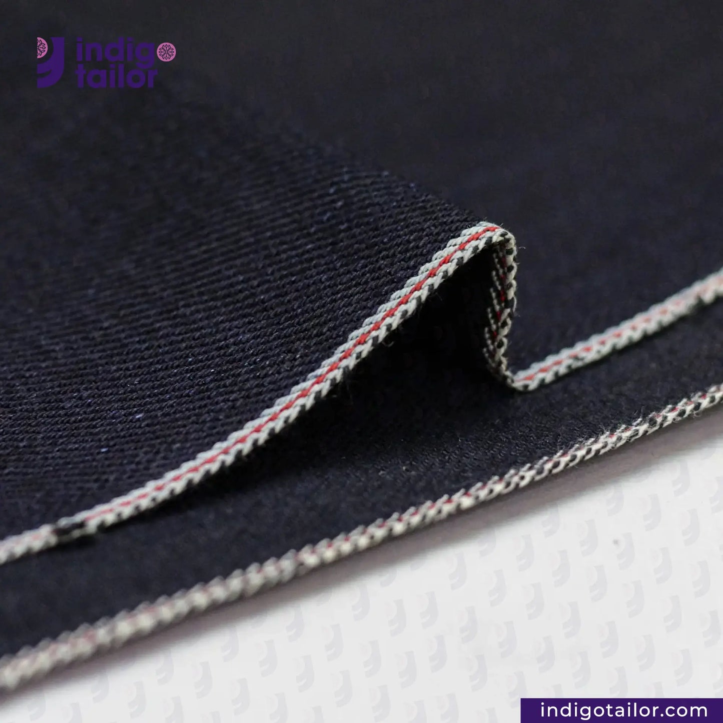 Close-up of INDIGO X BLACK SELVEDGE DENIM fabric with a visible brand logo on a white background