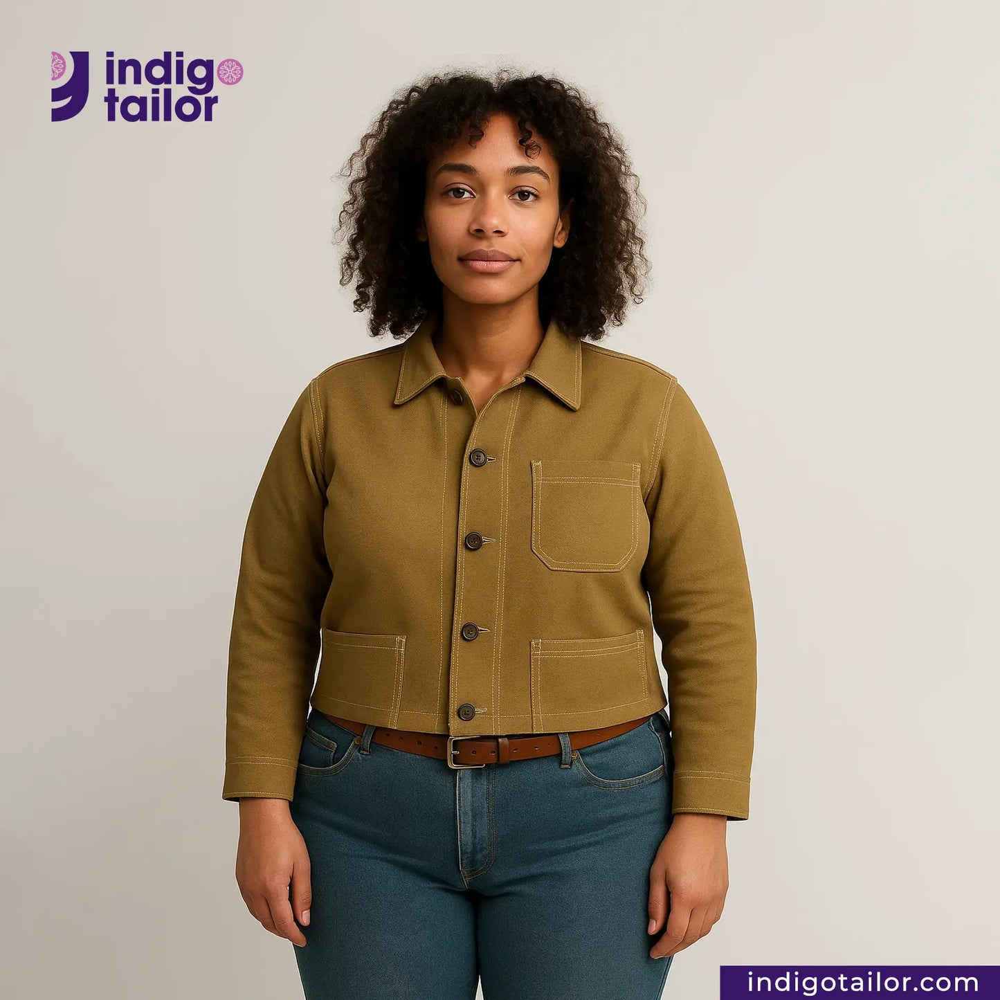 Woman wearing a KHAKI HERRINGBONE COVERALL JACKET jacket and blue jeans with 'Indigo Tailor' logo.