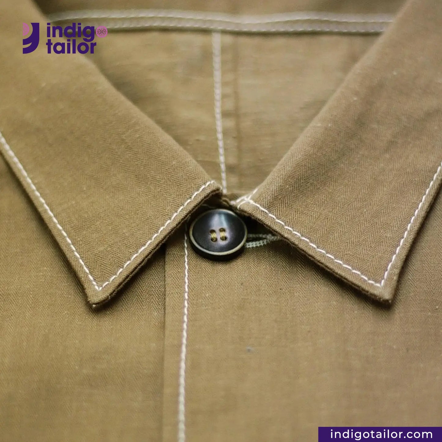 Close-up of a KHAKI HERRINGBONE COVERALL JACKET collar with a button, featuring 'indig tailor' branding.