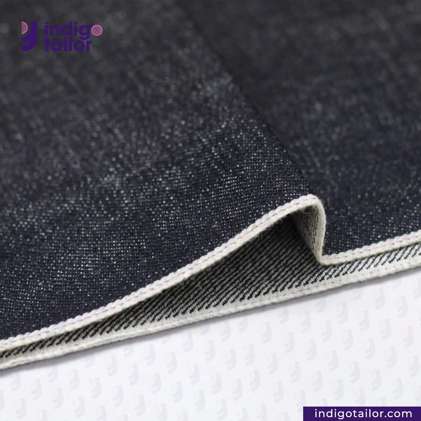 Close-up of KUROKI SLUBBY AND HEAVY DEEP INDIGO PINK SELVEDGE fabric with a visible brand logo, on a white background.