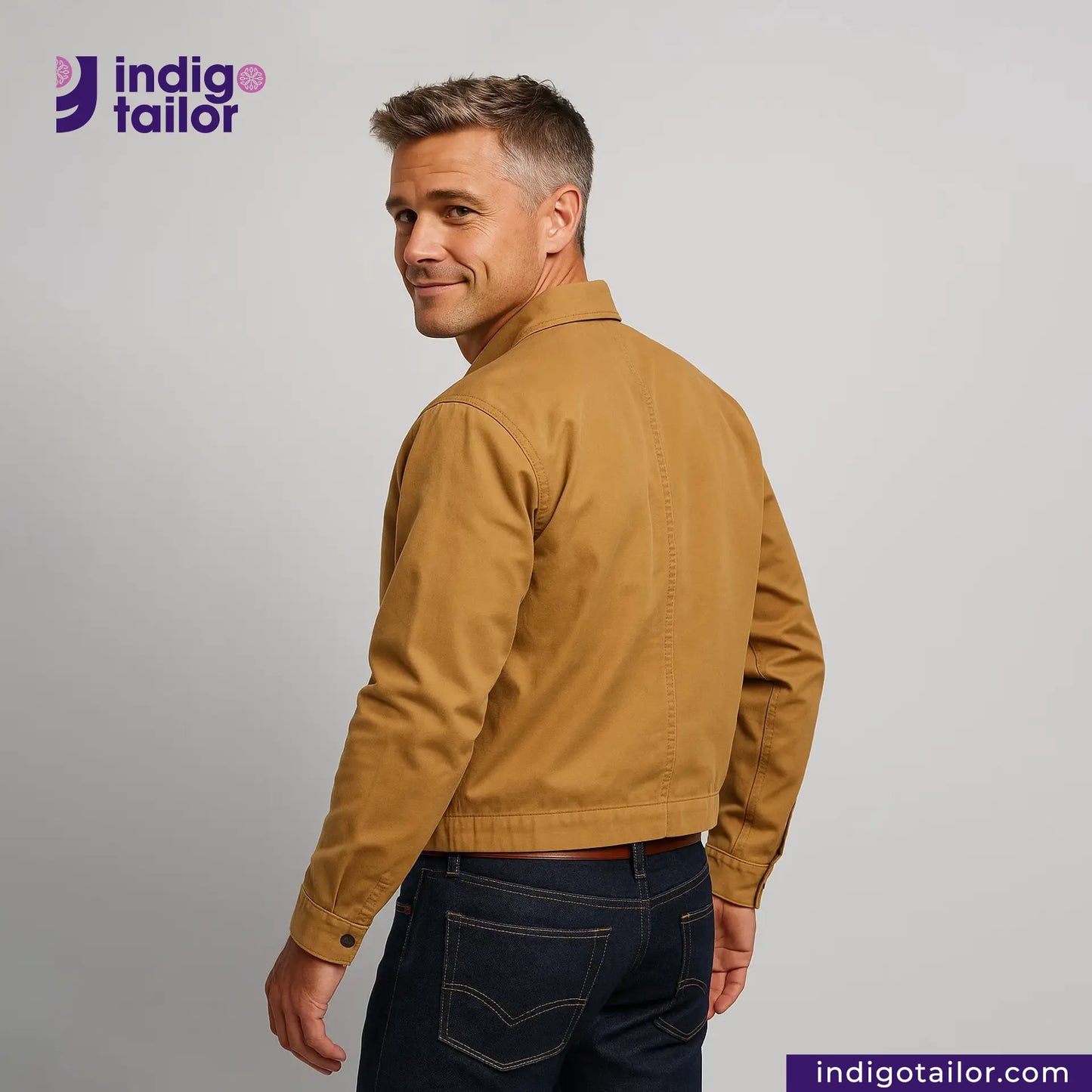 Man wearing a Khaki Bomber Jacket and dark jeans, standing against a gray background with 'indigotailor' branding.