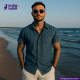 Man wearing a OCEAN BLUE COTTON HEMP BLEND SELVEDGE DENIM shirt and sunglasses on a beach with 'indigotailor' branding.