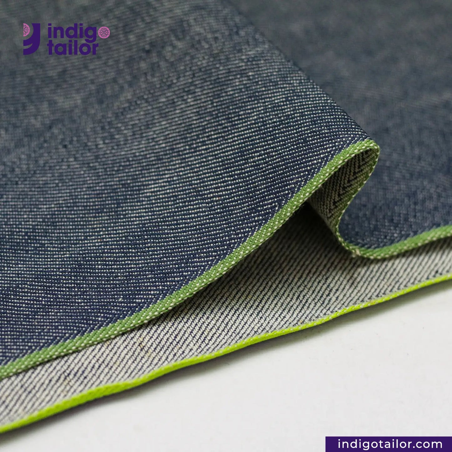 Close-up of OCEAN BLUE COTTON HEMP BLEND SELVEDGE DENIM fabric with green edge, featuring 'indigotailor' brand.