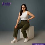 Woman sitting on a white cube wearing a white tank top and Olive Green Corduroy pants, with 'Indigotailor' branding.