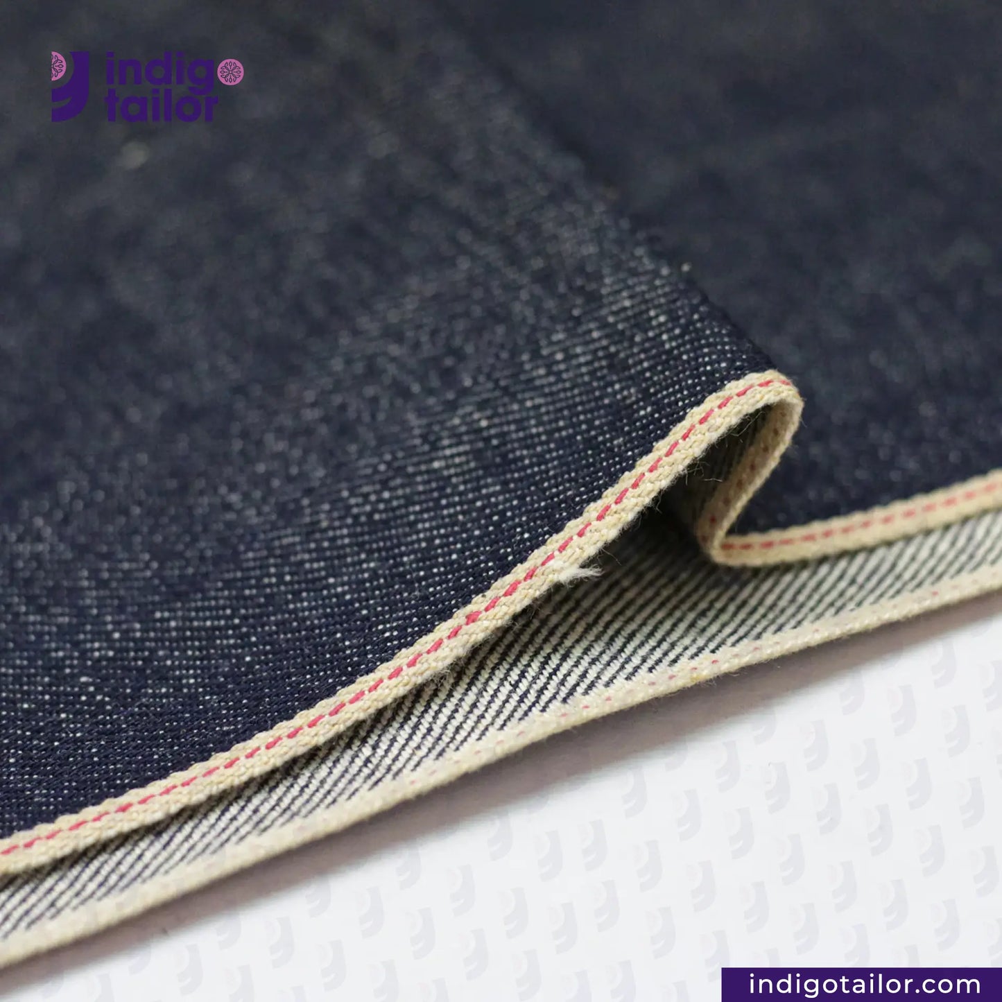 Close-up of RIGID INDIGO SELVEDGE DENIM fabric with visible stitching, featuring the Indigotailor logo.