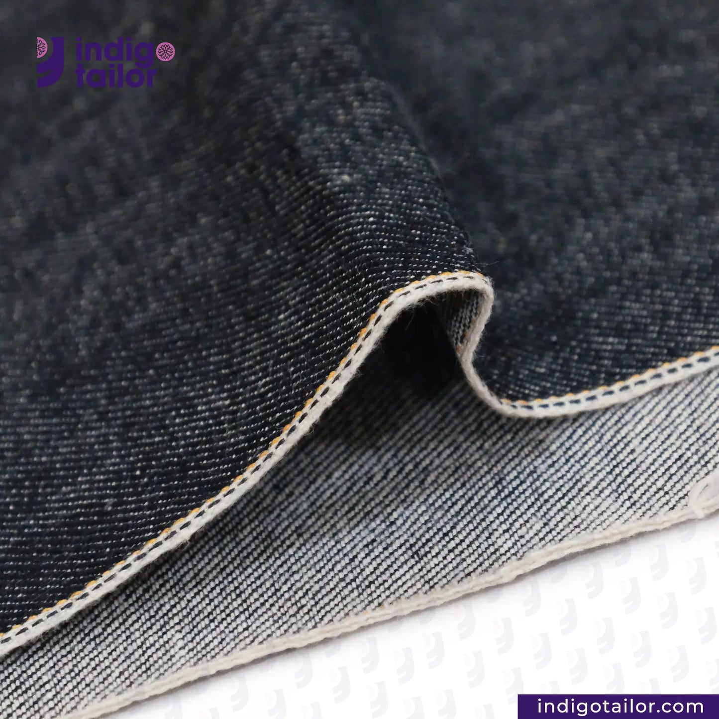 Close-up of ROUGH-SPUN DENIM FUZZY HANDFEEL fabric with visible stitching, featuring the Indigo Tailor logo.