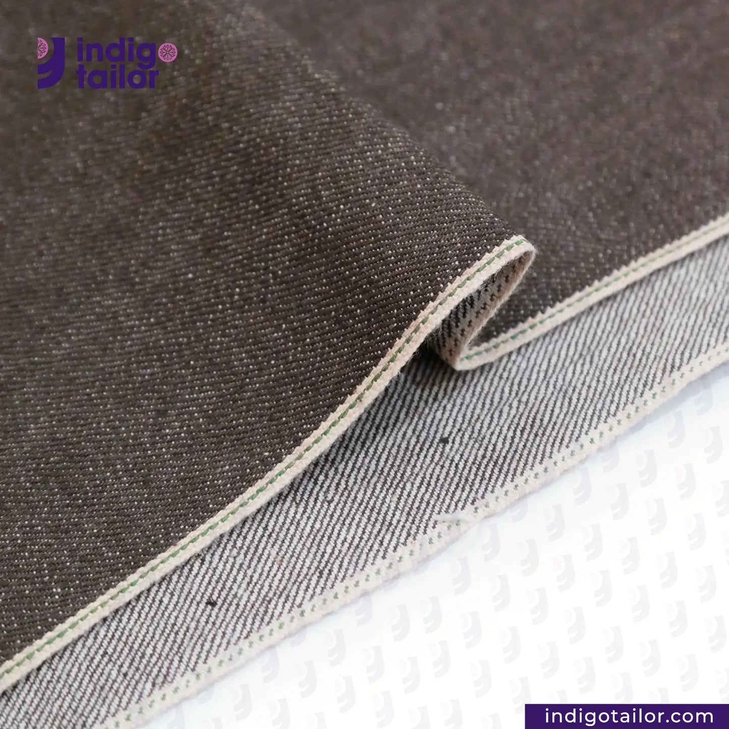 Close-up of SLUBBY BROWN SELVEDGE DENIM fabric with 'Indigo Tailor' logo and website URL.