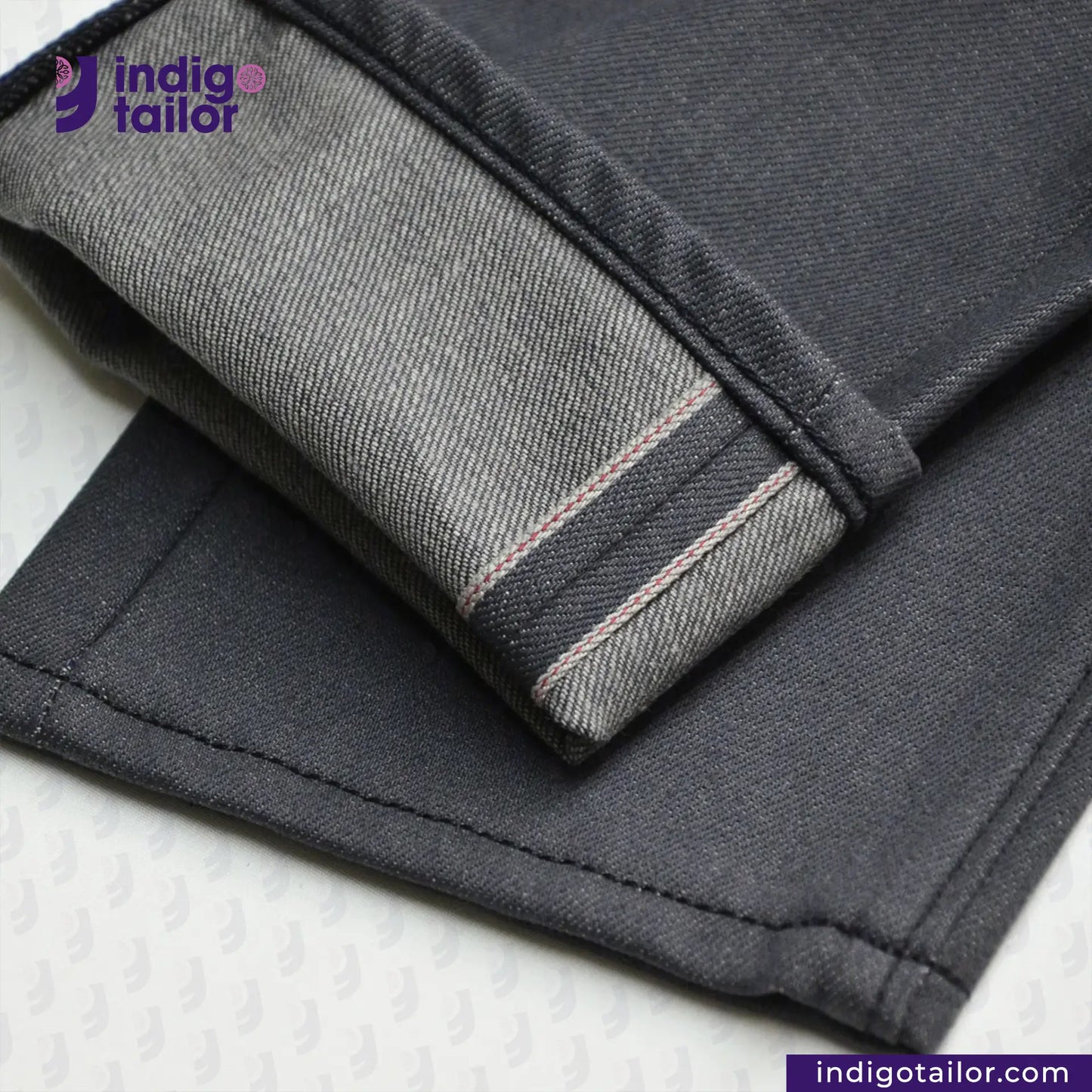 Close-up of SMOKE GREY DENIM jeans with a visible brand logo on a light background