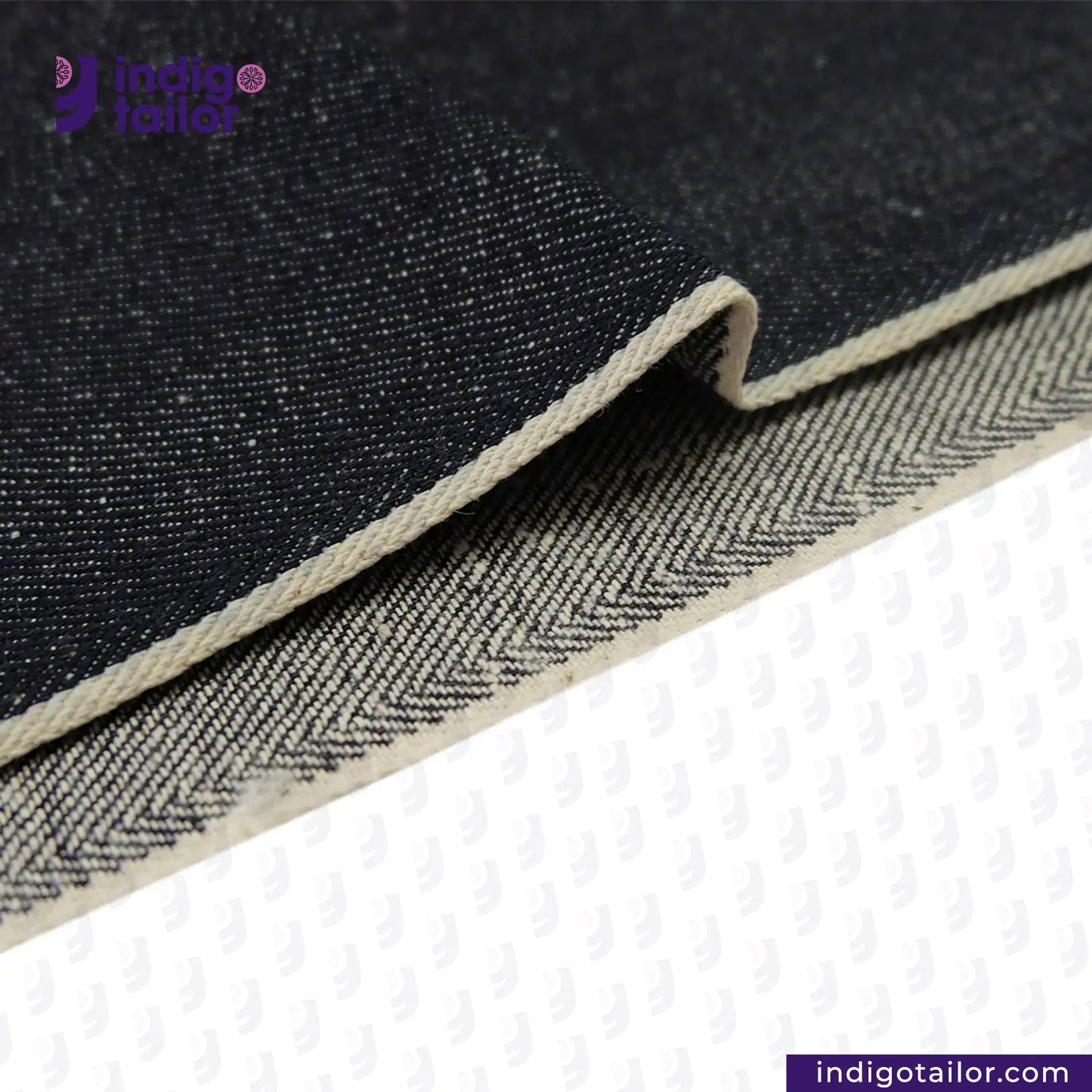 Close-up of SNOWY NEPPY WHITE SELVEDGE DENIM fabric with a herringbone pattern, featuring the Indigo Tailor logo.