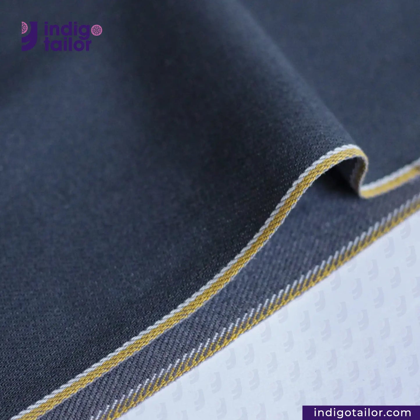 Close-up of SPACE GREY DENIM fabric with yellow stitching, featuring Indigotailor logo.