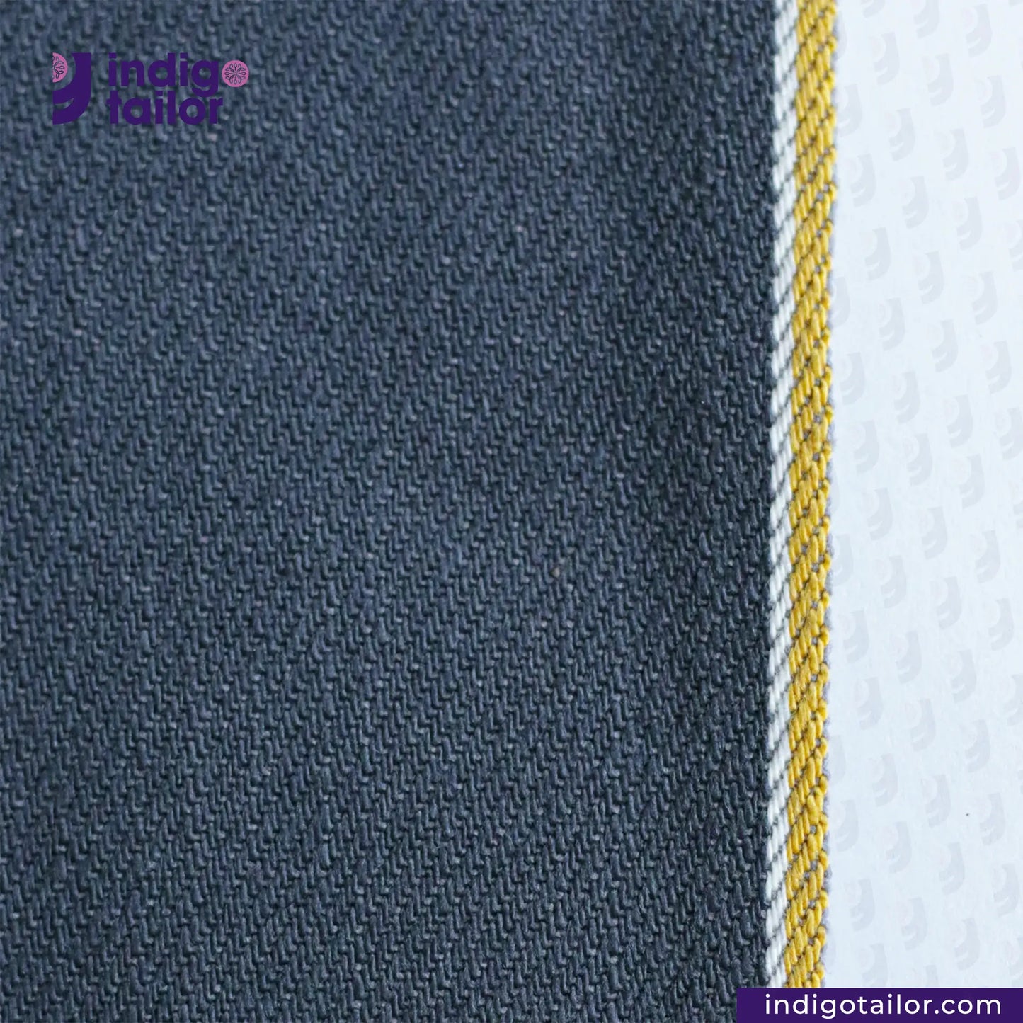 Close-up of SPACE GREY DENIM fabric with a striped pattern featuring blue, yellow, and white sections, branded 'Indigo Tailor'.