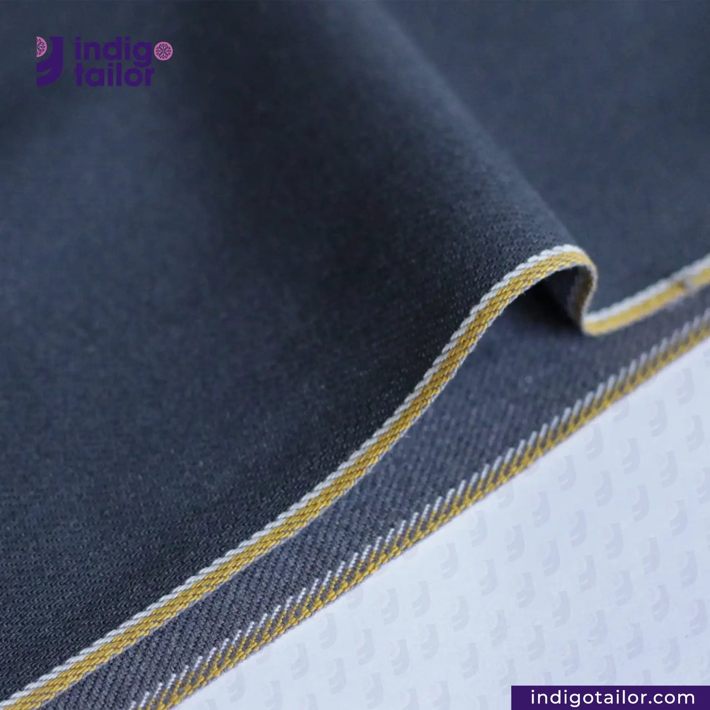 Close-up of SPACE GREY DENIM fabric with yellow stitching, featuring Indigotailor logo.