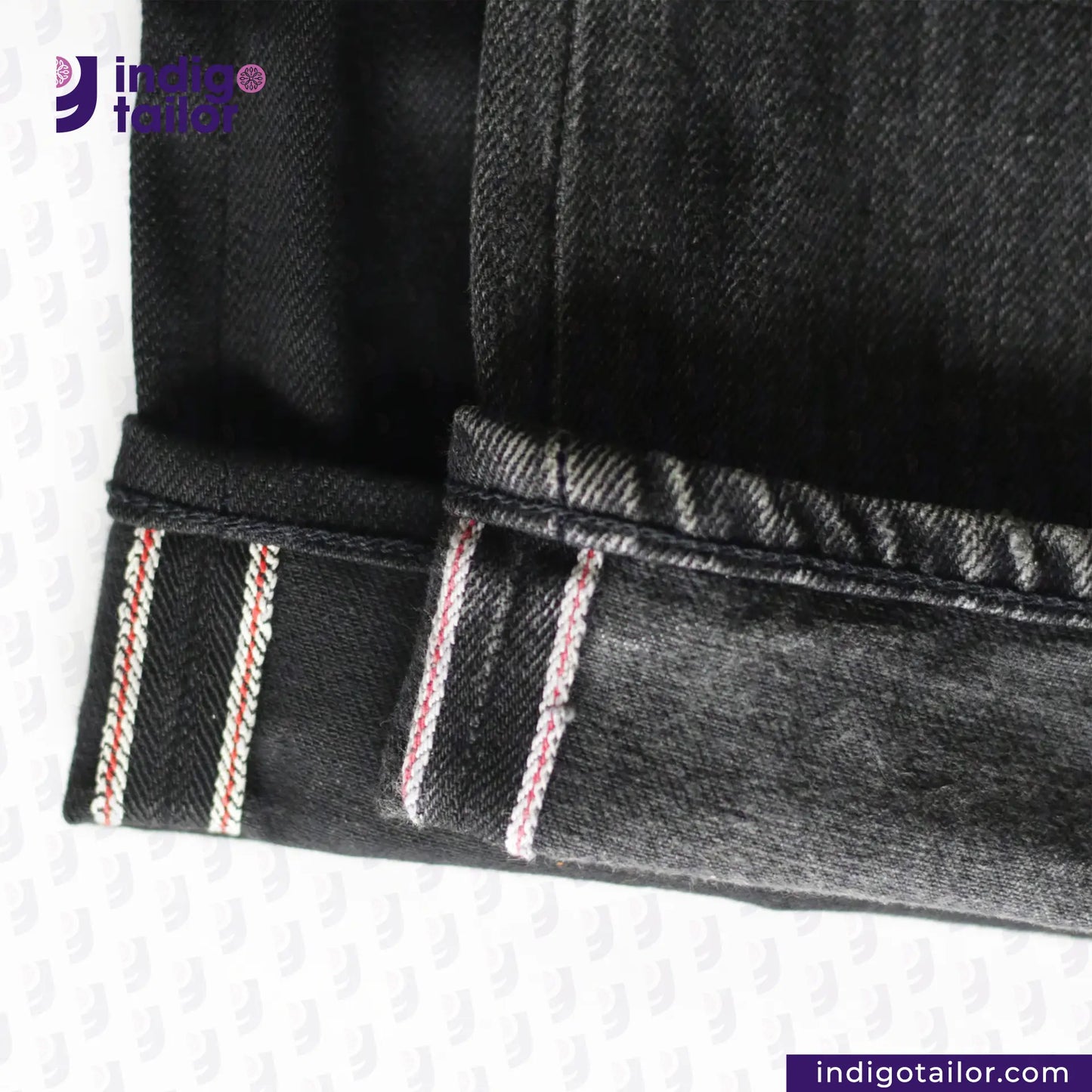 Close-up of SUPER BLACK DENIM jeans with red and white stitching on a white background, featuring the 'Indigo Tailor' brand.