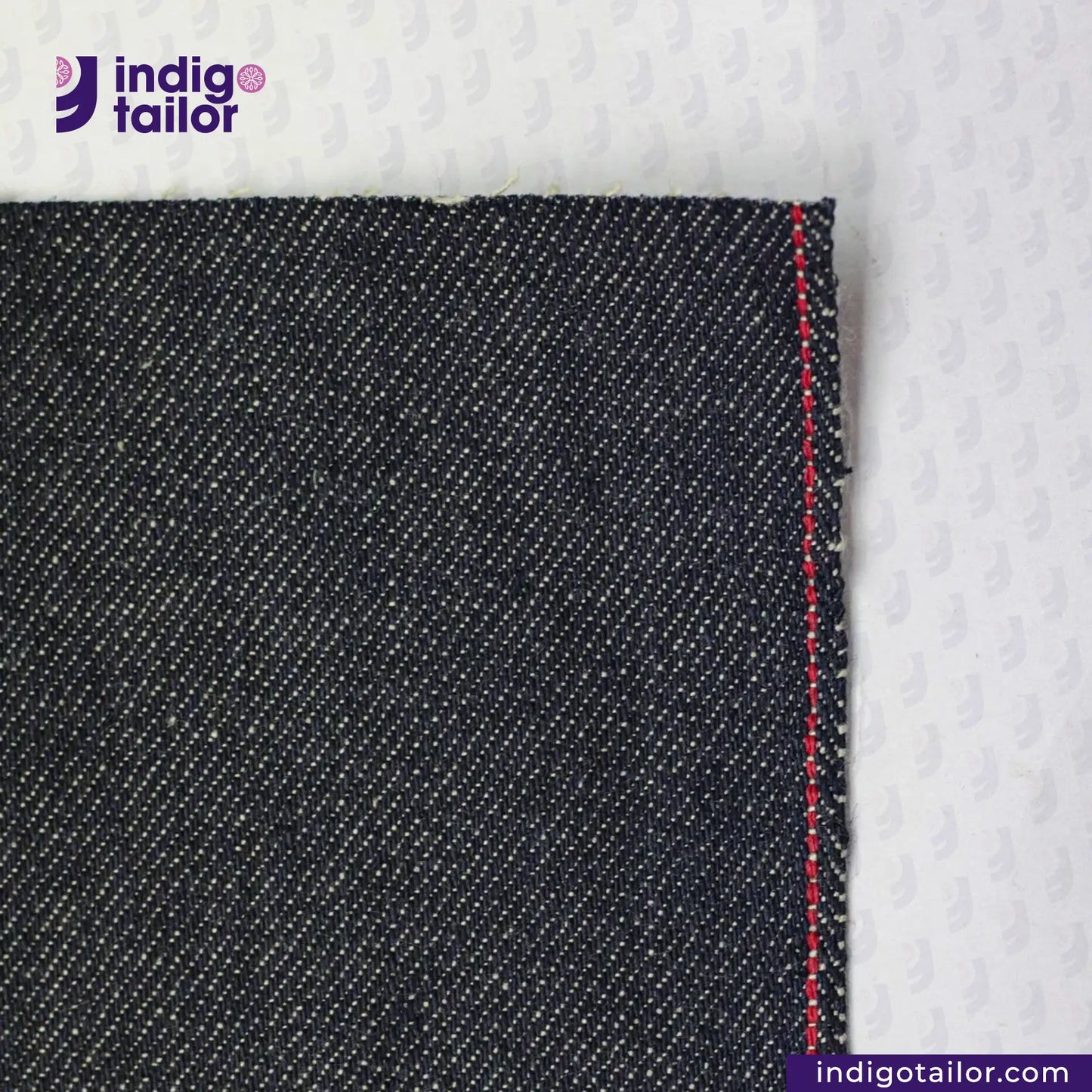 Close-up of TATE OCHI DOUBLE RING SPUN SELVEDGE DENIM fabric with a red stitch on a white background, featuring the Indigotailor logo.