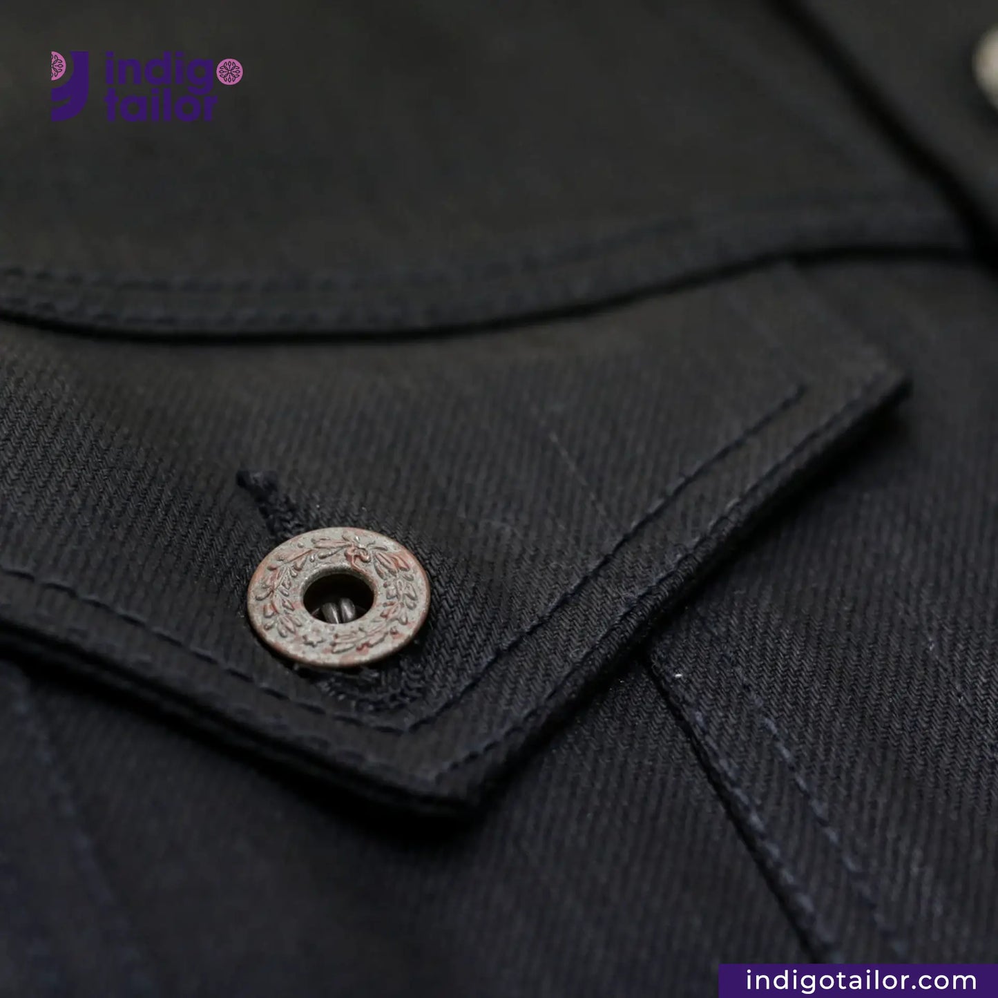 Close-up of a button on a TYPE III DOUBLE BLACK TRUCKER JACKET garment with 'Indigo Tailor' branding.