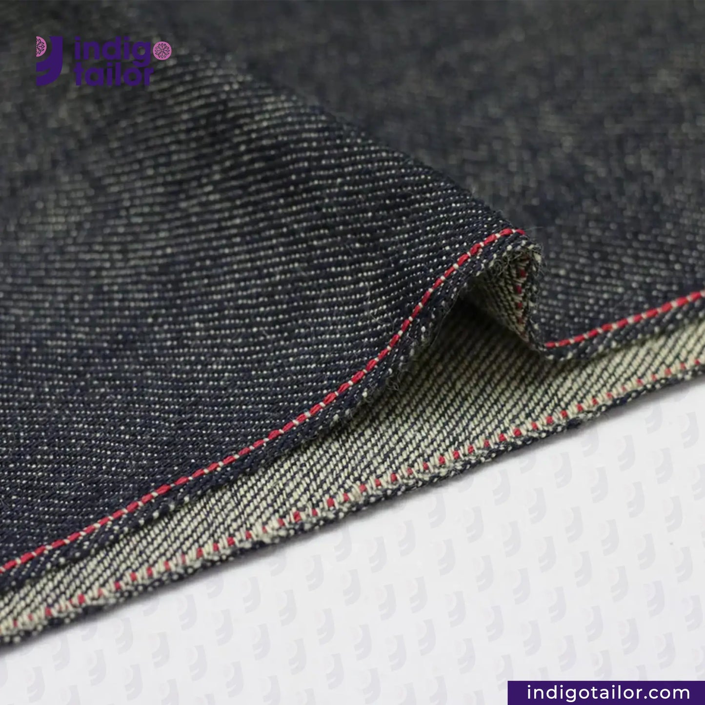 Close-up of UNSANFORIZED LOOM-STATE KIBATA DENIM fabric with visible stitching on a white background, featuring the Indigo Tailor logo.