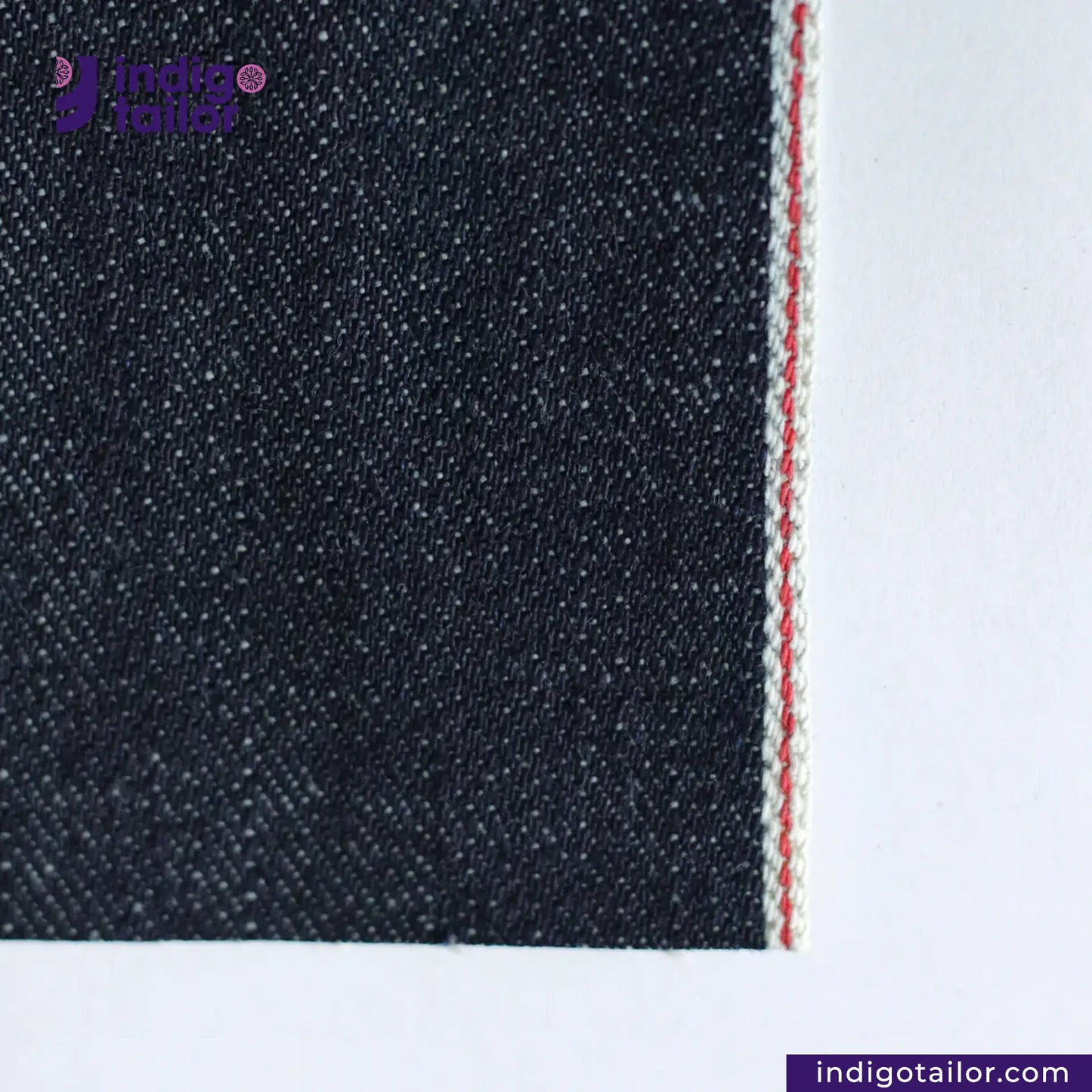 Close-up of VINTAGE SLUB DENIM fabric with a visible seam on a white background, featuring the Indigo Tailor logo.