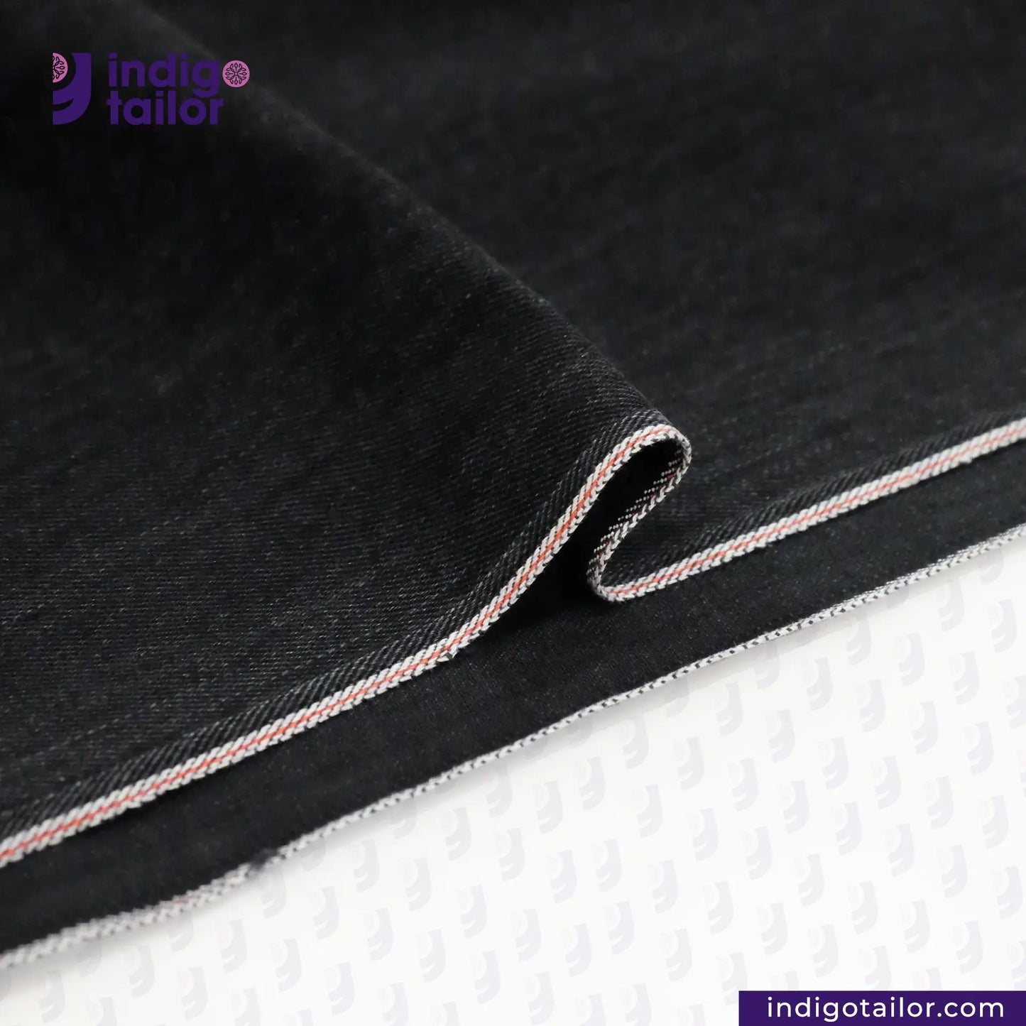 Close-up of WASHED BLACK x BLACK SELVEDGE denim fabric with white stitching on a white background, featuring the Indigotailor logo.