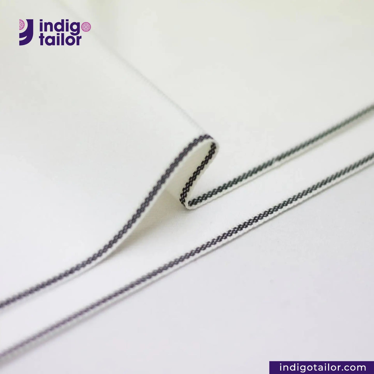 WHITE DENIM BLACK SELVEDGE, Close-up of a white fabric with black stitching, featuring the Indigotailor logo.