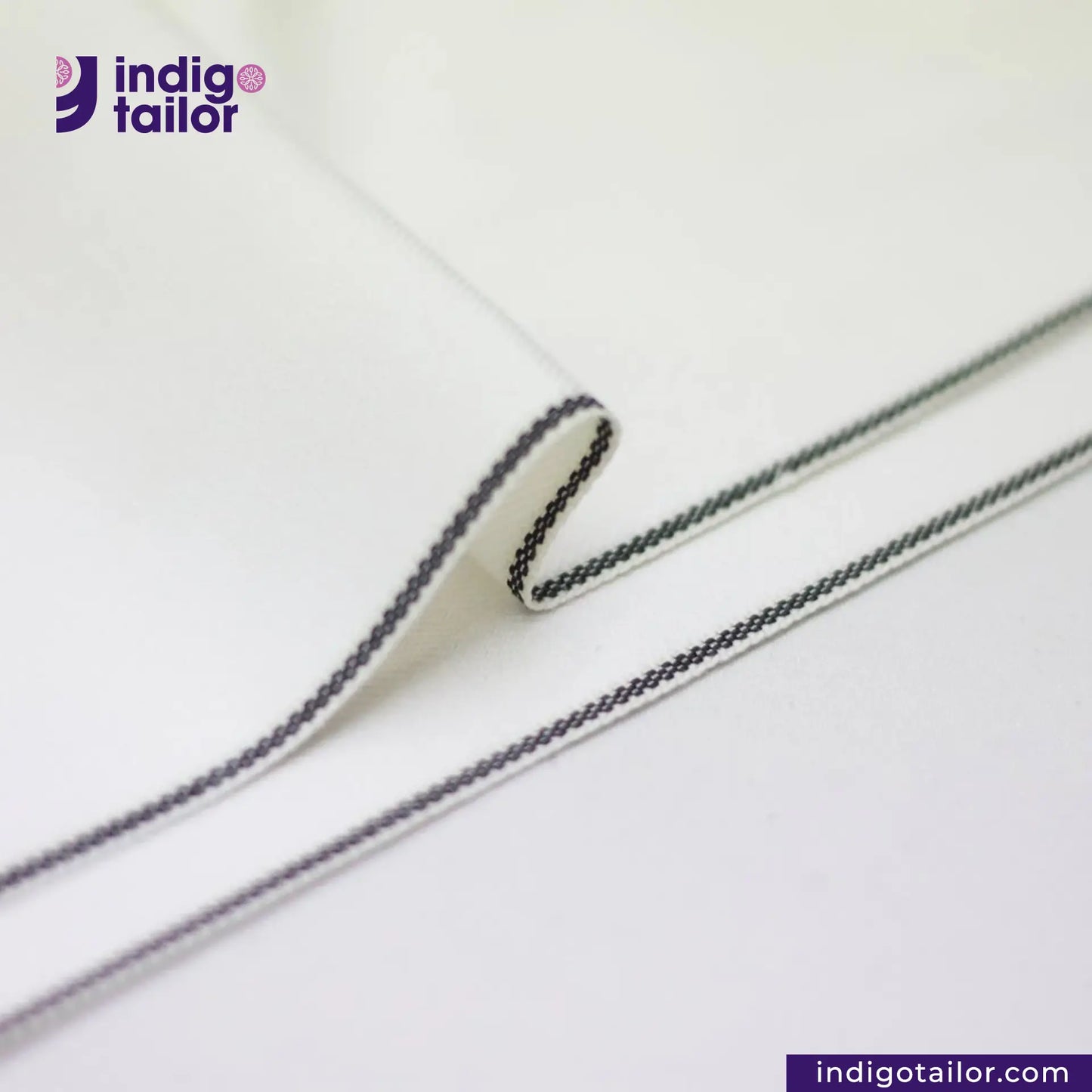 Close-up of WHITE DENIM BLACK SELVEDGE fabric with black thread stitching, featuring the Indigotailor logo.