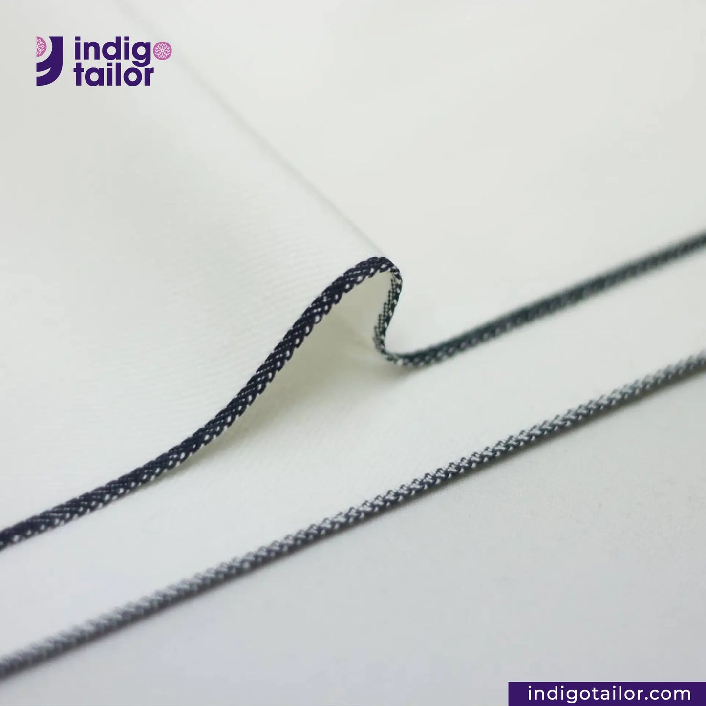 Close-up of WHITE DENIM NAVY SELVEDGE fabric with 'indigotailor' branding on a white background