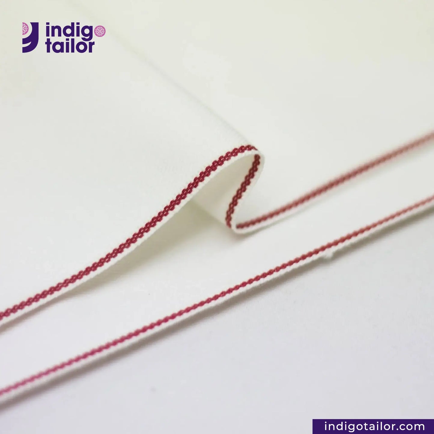 Close-up of a WHITE DENIM RED SELVEDGE fabric edge with red stitching on a white background, featuring the Indigotailor logo.