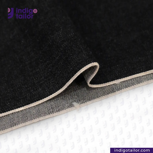 Close-up of BLACK SLUBBY SELVEDGE DENIM fabric with beige edge on a white background, featuring Indigotailor logo.