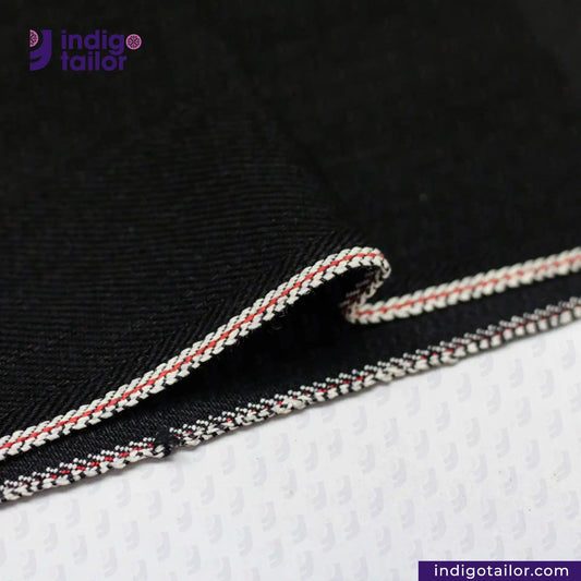 Close-up of BLACK X BLACK SELVEDGE DENIM fabric with white and red trim, branded 'Indigotailor'.